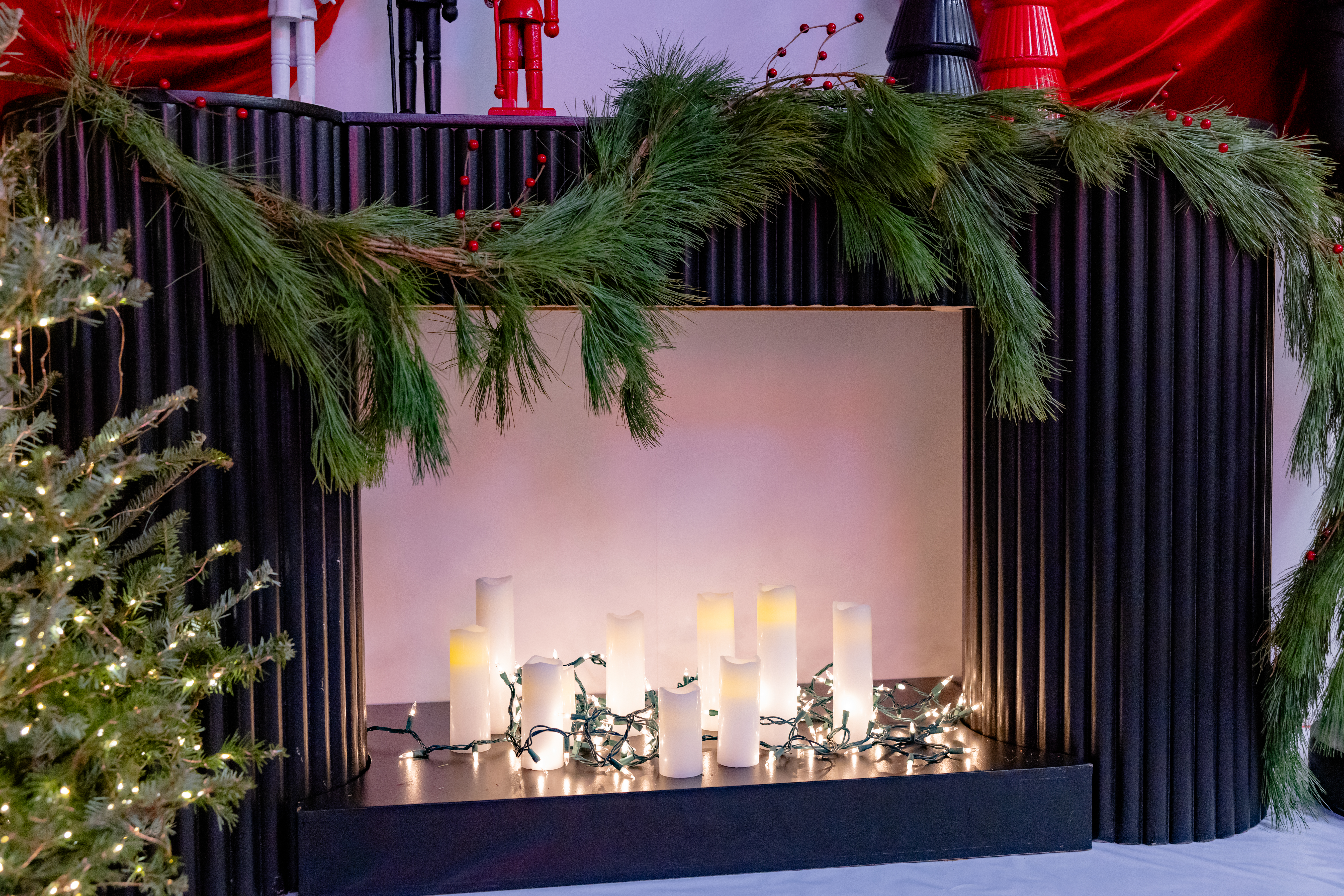 a picture of a fireplace set for the holiday season with candles, garland and you can see the bottom of nutcrackers and little figurine trees